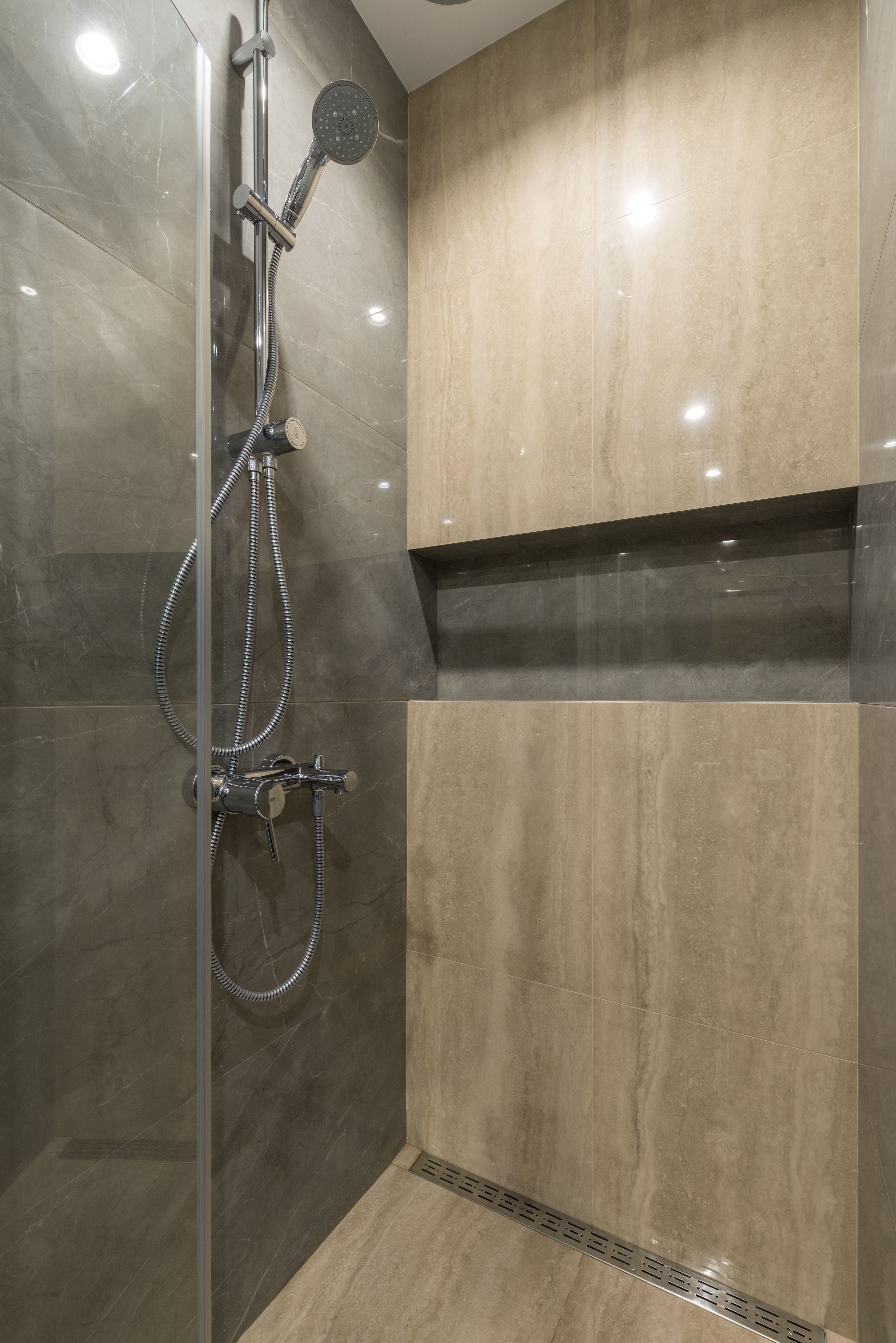 Shower stall with chrome fixtures and tiled walls in a bathroom.