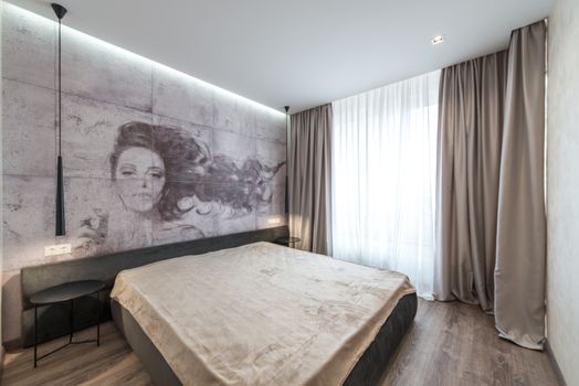 Cozy bed with small tables placed near wall with creative wallpaper with woman painting in modern bedroom decorated with lamps and silk curtains