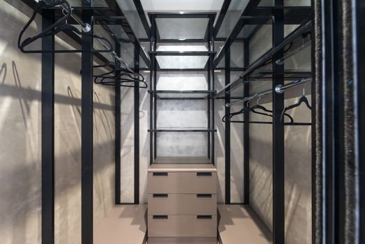 Built in closet with chest of drawers placed between empty racks with hangers