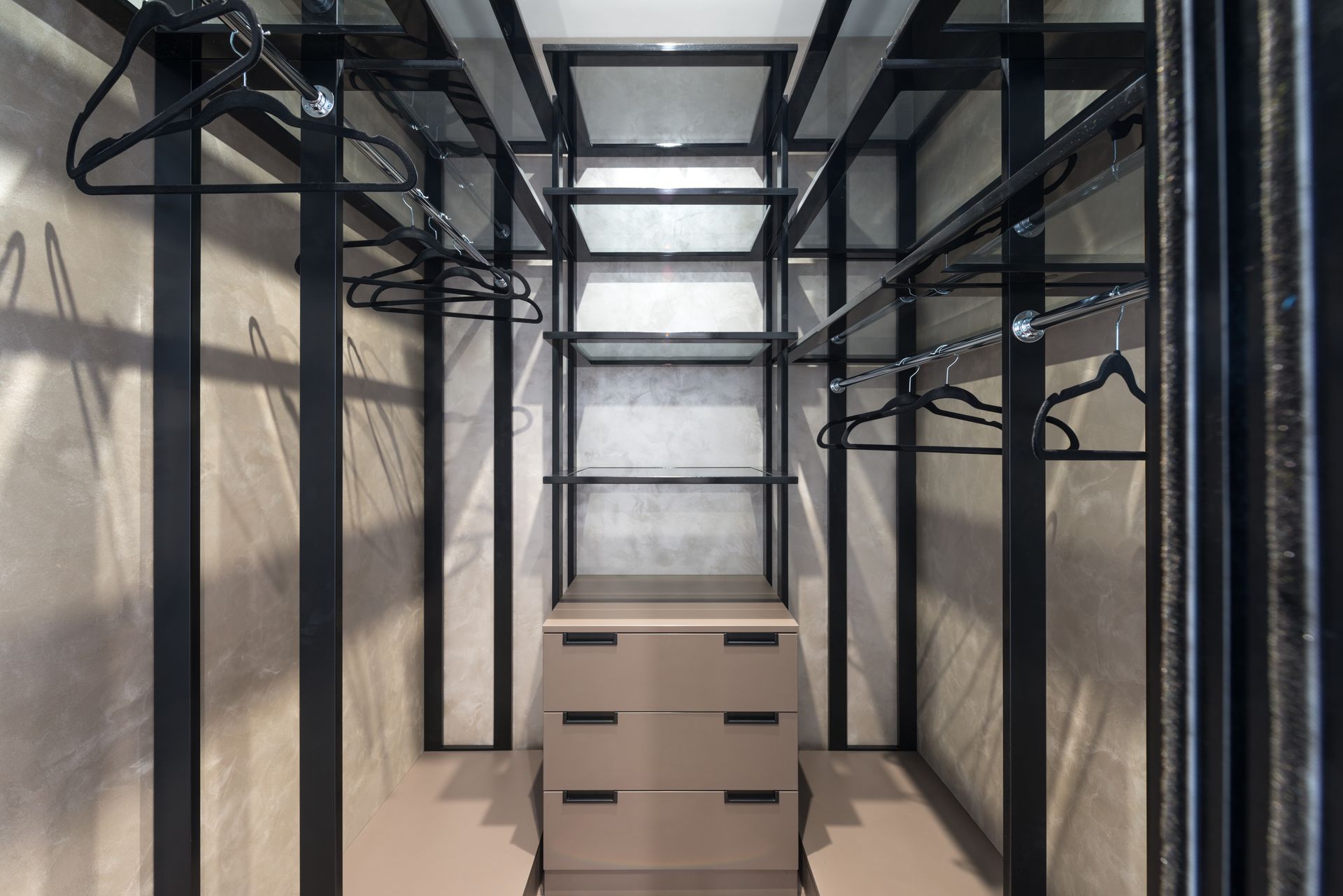 Built in closet with chest of drawers placed between empty racks with hangers