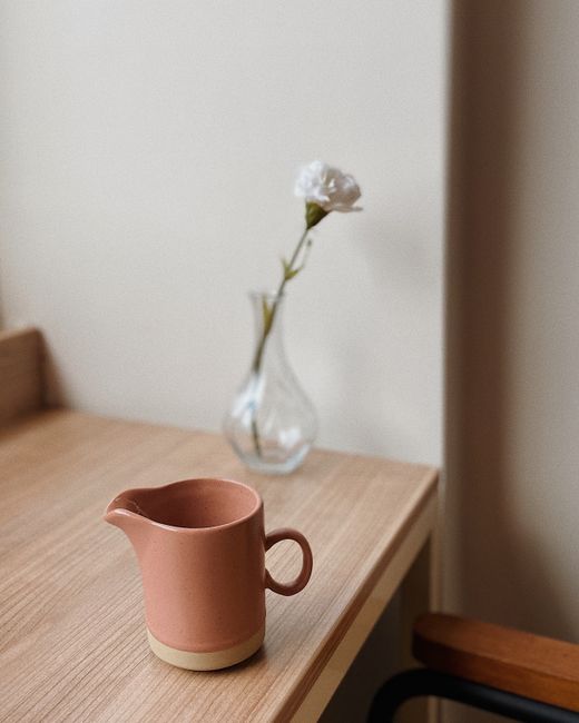 Simple wooden table featuring a ceramic jug and a single flower in a vase for a minimalist décor.