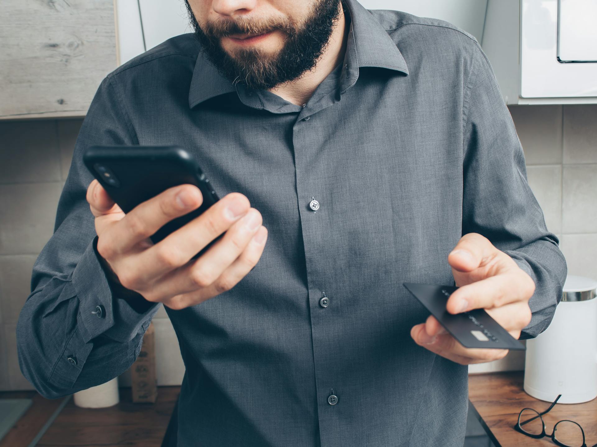 Close-up of a man using a smartphone for online payment with a credit card indoors.