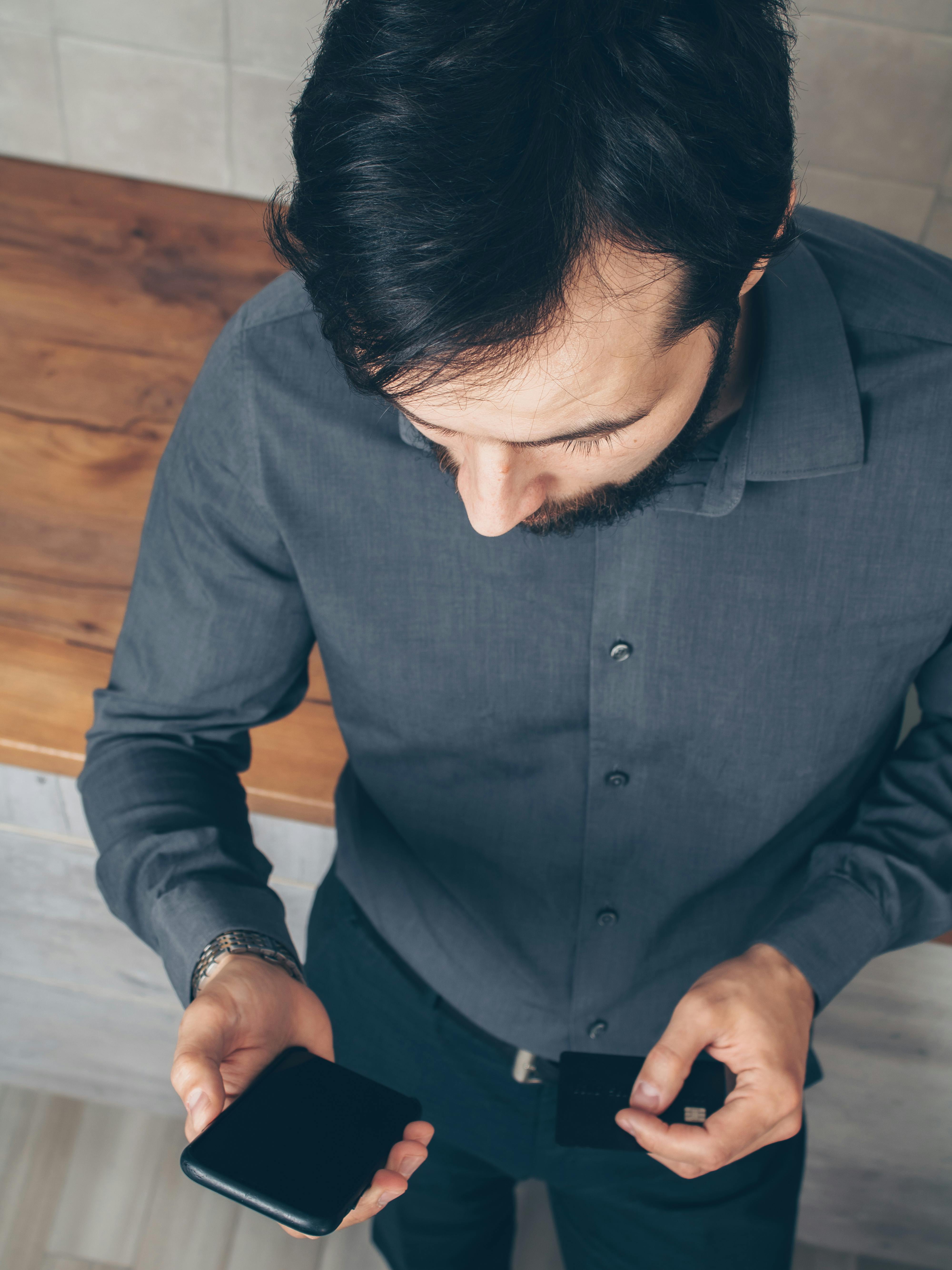 man in gray dress shirt holding black smartphone