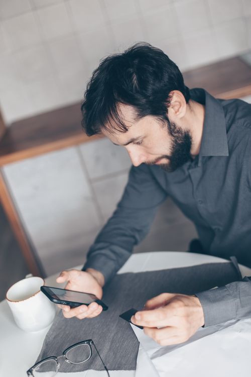 Free Focused young man sitting at desk using smartphone for online payment, indoor setting. Stock Photo