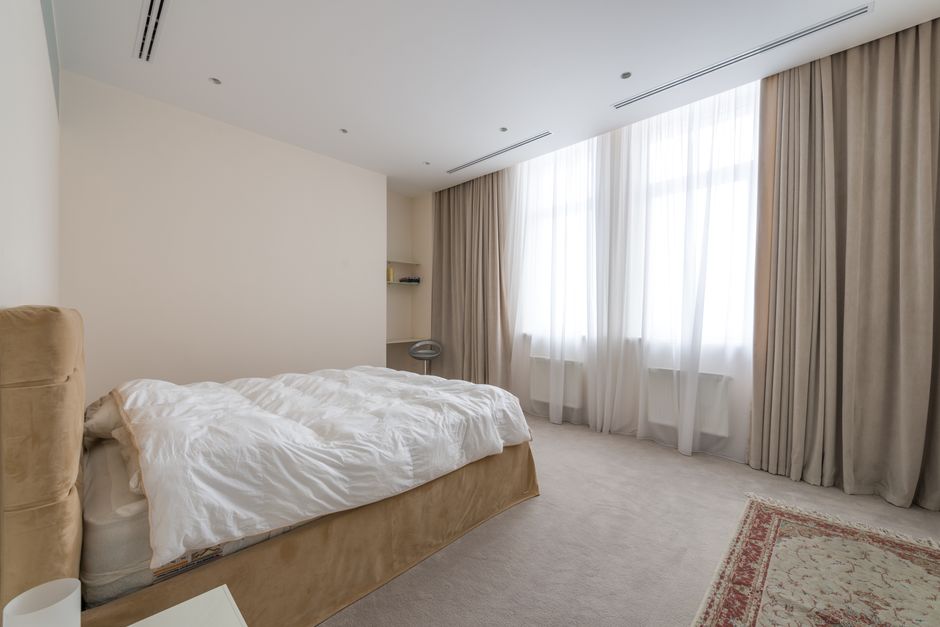 Modernes Schlafzimmer mit beigen Verdunkelungsvorhängen, hellem Holz und ruhiger Wandfarbe als Beispiel für Schlafzimmer abdunkeln.
