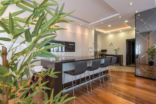 Kitchen island with black leather chairs in spacious modern apartment with white minimalist furniture and built in appliances