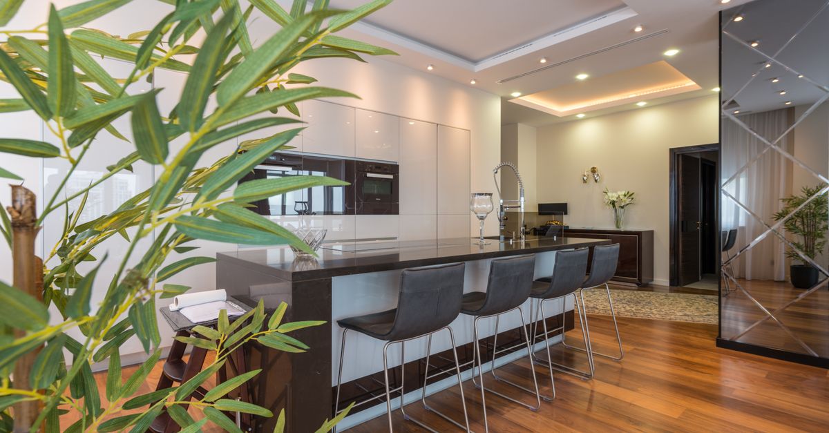 Kitchen island with black leather chairs in spacious modern apartment with white minimalist furniture and built in appliances