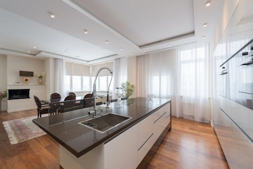 Interior of contemporary kitchen with modern white furniture and sink in island in spacious elegant apartment in daylight