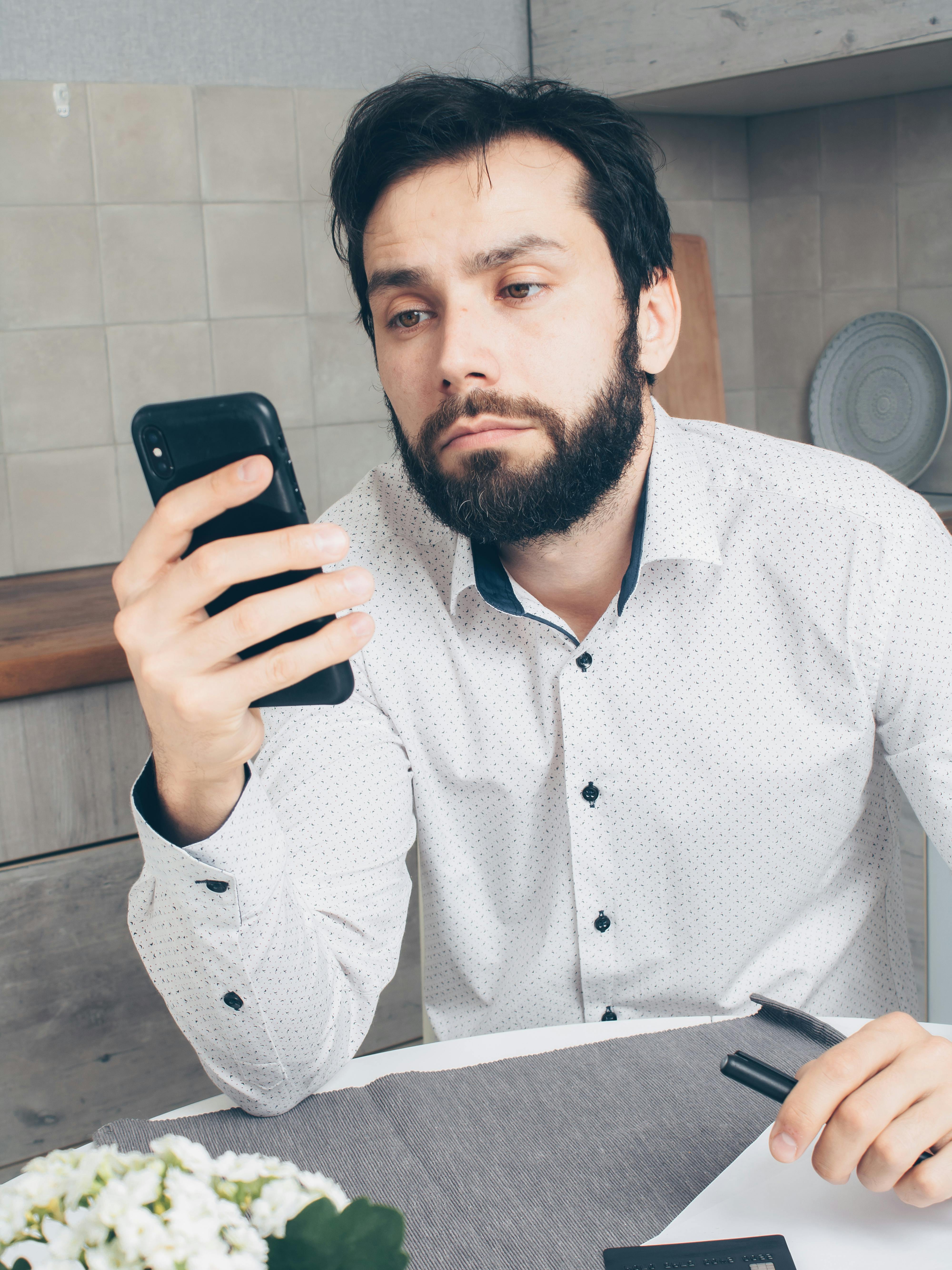 man in white and black polka dot dress shirt holding black smartphone