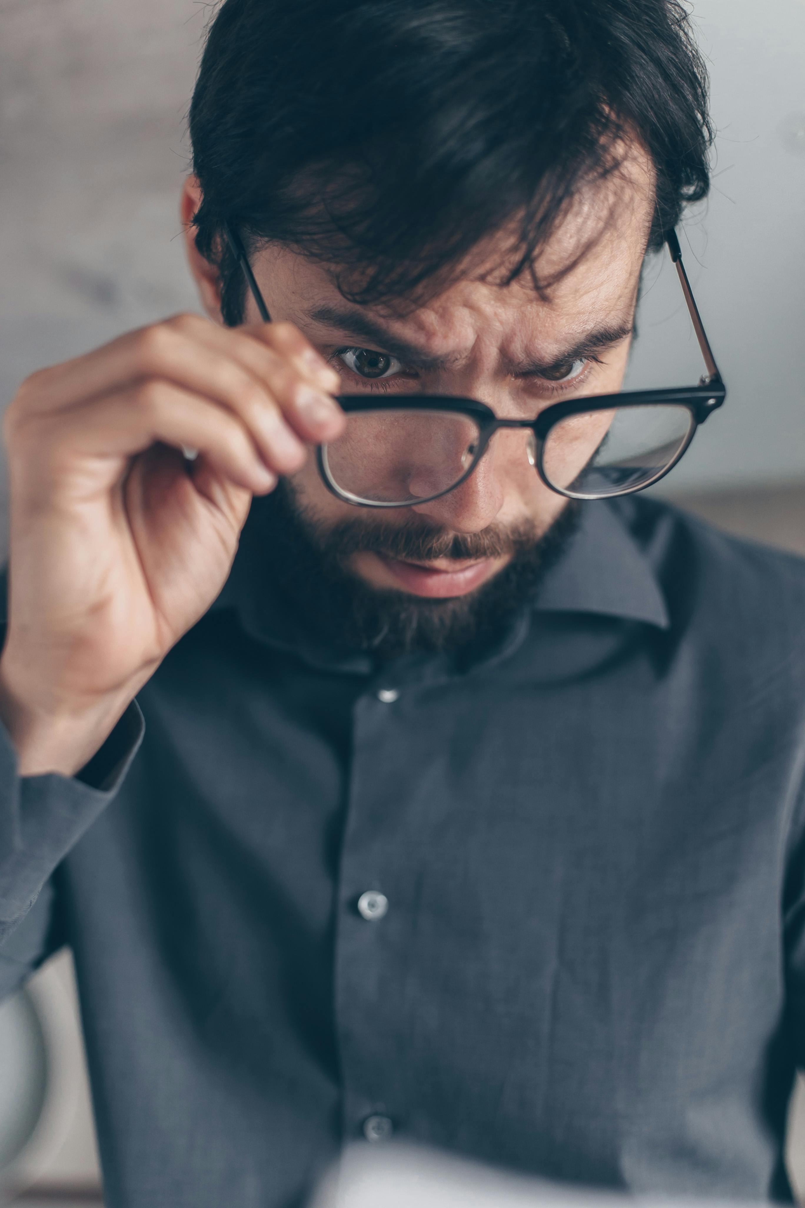 a man in gray long sleeves holding his eyeglasses