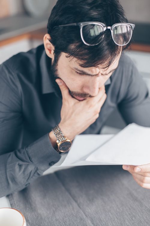 Free Man in gray shirt with glasses looking concerned over financial papers. Stock Photo