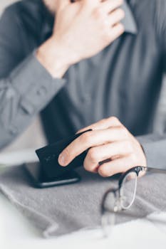 Close-up of a hand holding a credit card above a smartphone on a desk, emphasizing online payment concept.