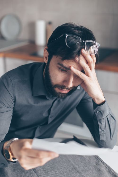 Free Man with eyeglasses on head looks worried as he reads paperwork, expressing concern. Stock Photo