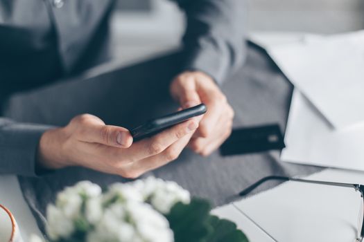 A close-up view of a man's hands using a smartphone with papers on a table.