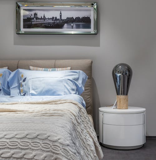 Interior of comfortable bedroom with gray walls and beige bed with light knitted coverlet and bedside table with modern lamp