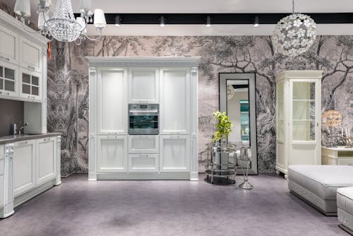 White cabinets with modern appliances placed in spacious kitchen with green plant and comfortable seats near decorative elements in apartment