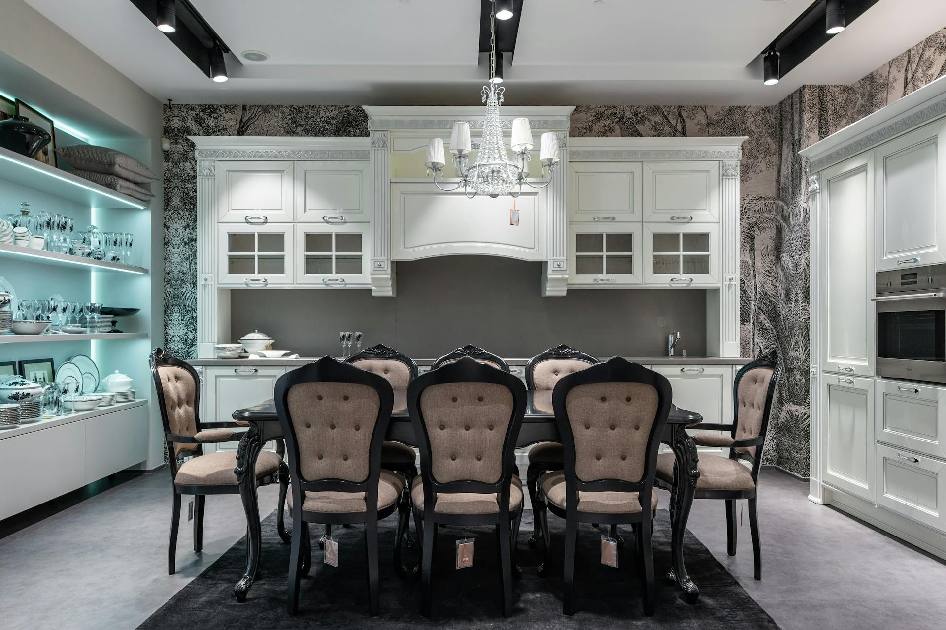 Chairs at table placed in spacious kitchen with oven near white cabinets and storage cupboard with various tableware in apartment