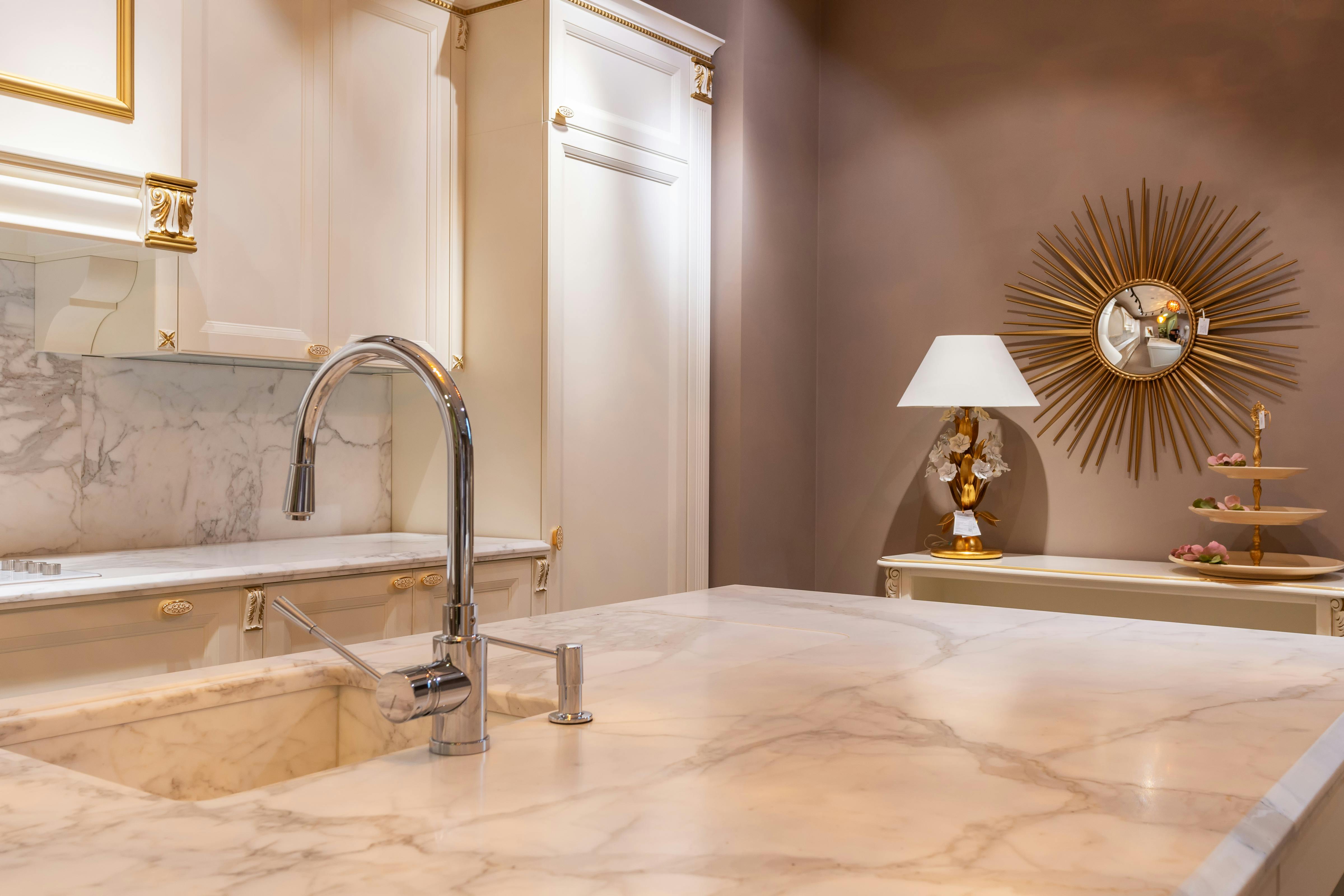 Sink with faucet on marble counter in modern stylish kitchen with white cabinets and glowing lamp near decorations in apartment