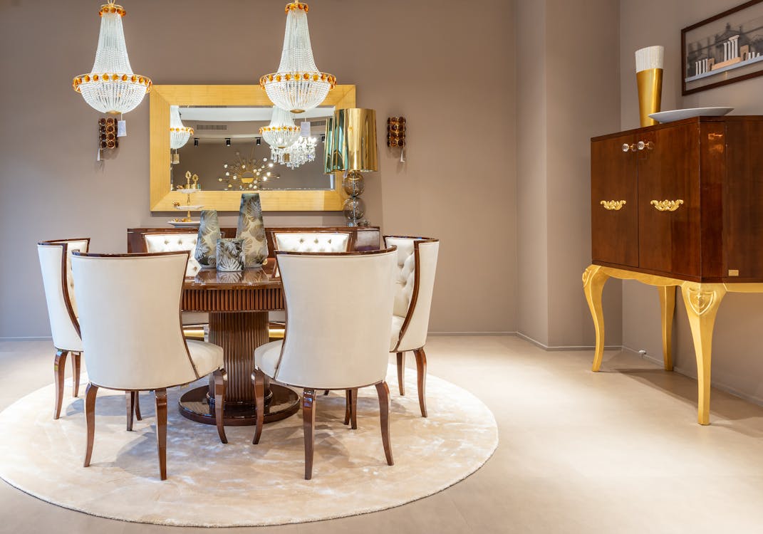 Chairs at round wooden table with decorative vases on placed on rug near wall with mirror in spacious apartment with cabinet