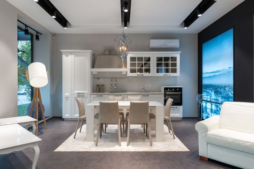 Free Chairs at table placed on rug near white cupboards and modern appliances at stylish kitchen with window and glowing lamp Stock Photo