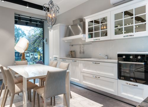 Free Table with chairs placed near white cupboards and modern appliances and utensils in light kitchen with glowing lamp near window Stock Photo