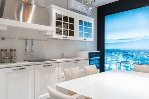 Free Table with chairs placed near white cupboards and counter with utensils and modern appliances in contemporary kitchen with window overlooking city Stock Photo
