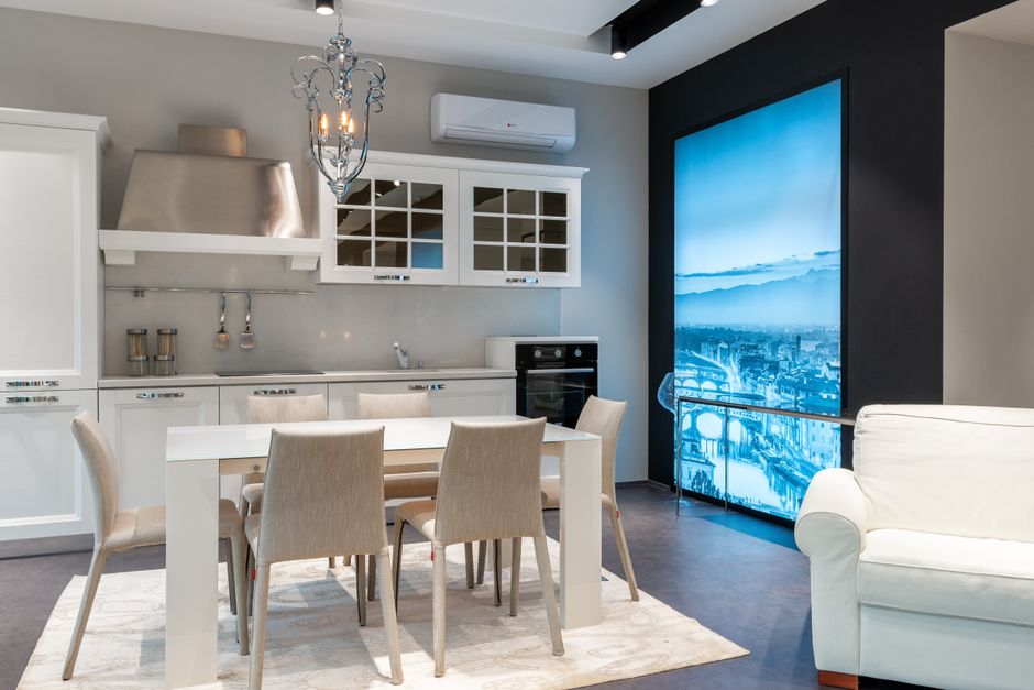 White dining table with soft chairs placed in spacious kitchen with elegant furniture and chandelier in modern studio apartment