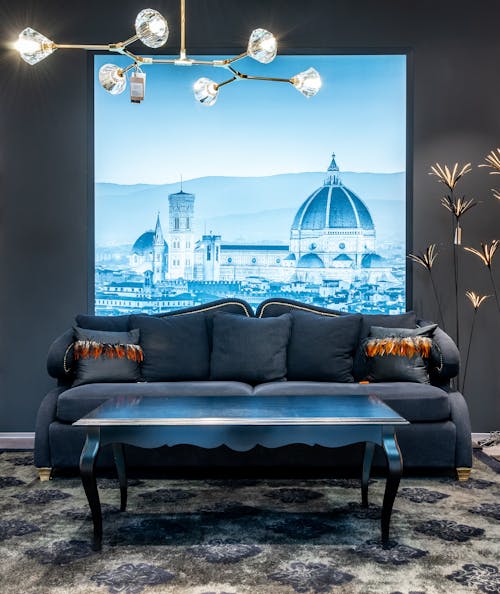 Comfortable elegant couch with cushions and coffee table placed in classic styled living room with chandelier and screen showing Cathedral of Santa Maria del Fiore