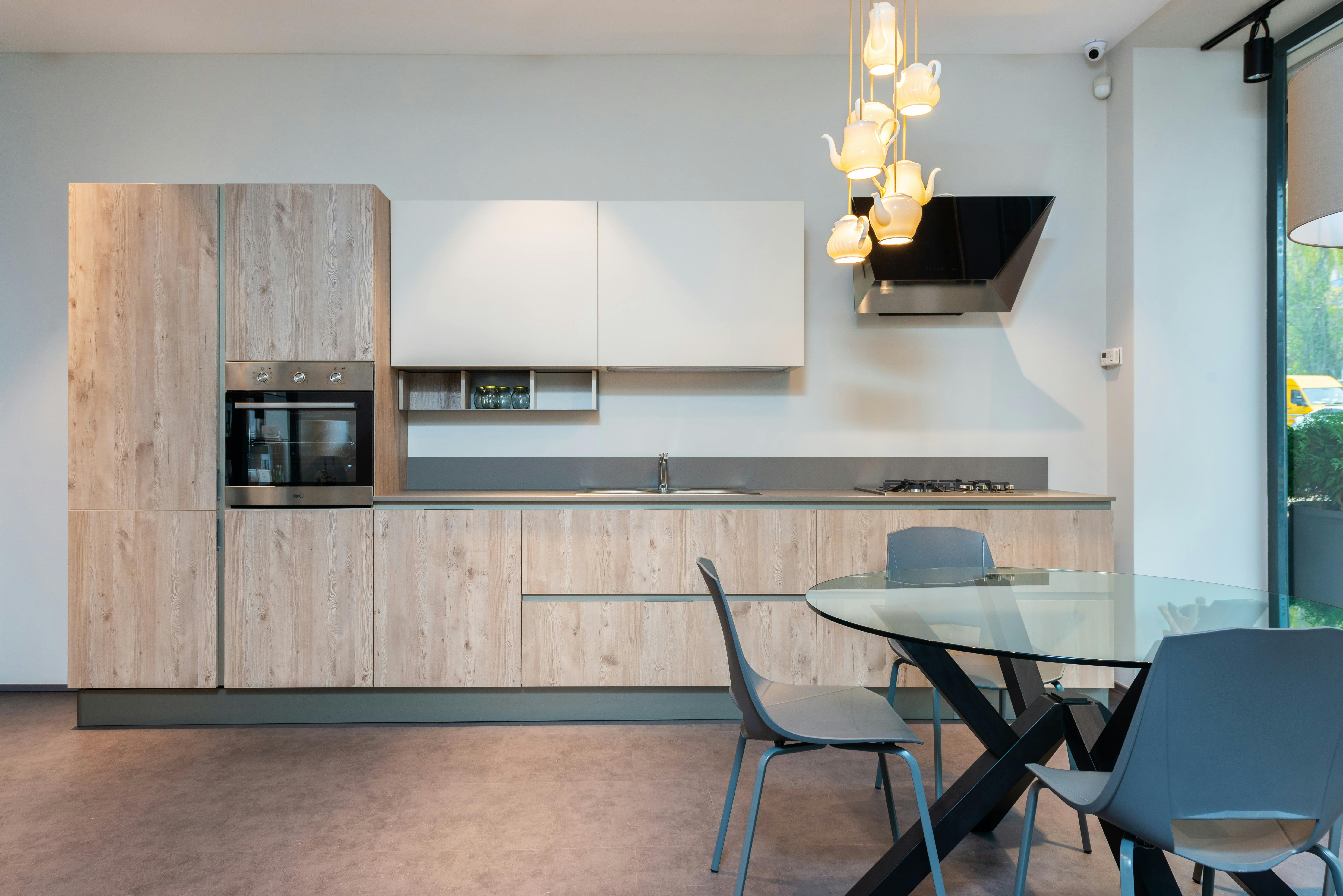 Stylish interior of spacious kitchen with light furniture and round glass dining table with chairs in modern apartment