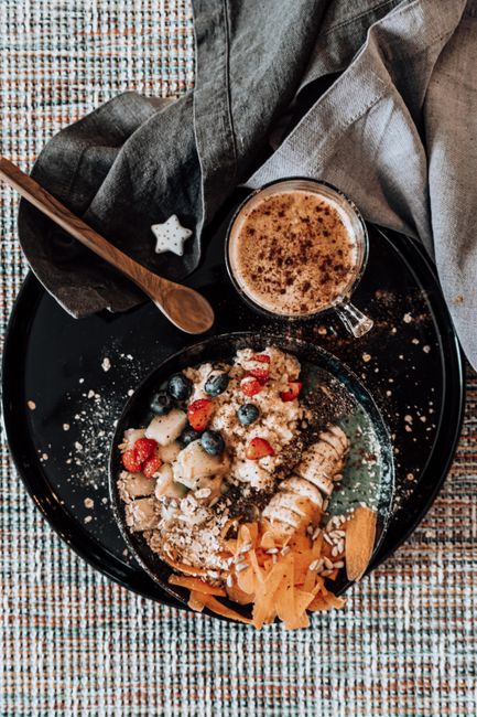 A tall glass of a pale brown-green smoothie topped with a swirl of peanut butter and a sprinkle of chia seeds, with a frozen banana and fresh spinach leaves arranged beside it on a wood counter.