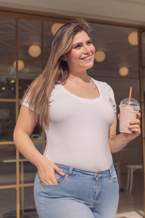 Free Smiling plus size woman in white tee holding a drink and enjoying a sunny day outside. Stock Photo