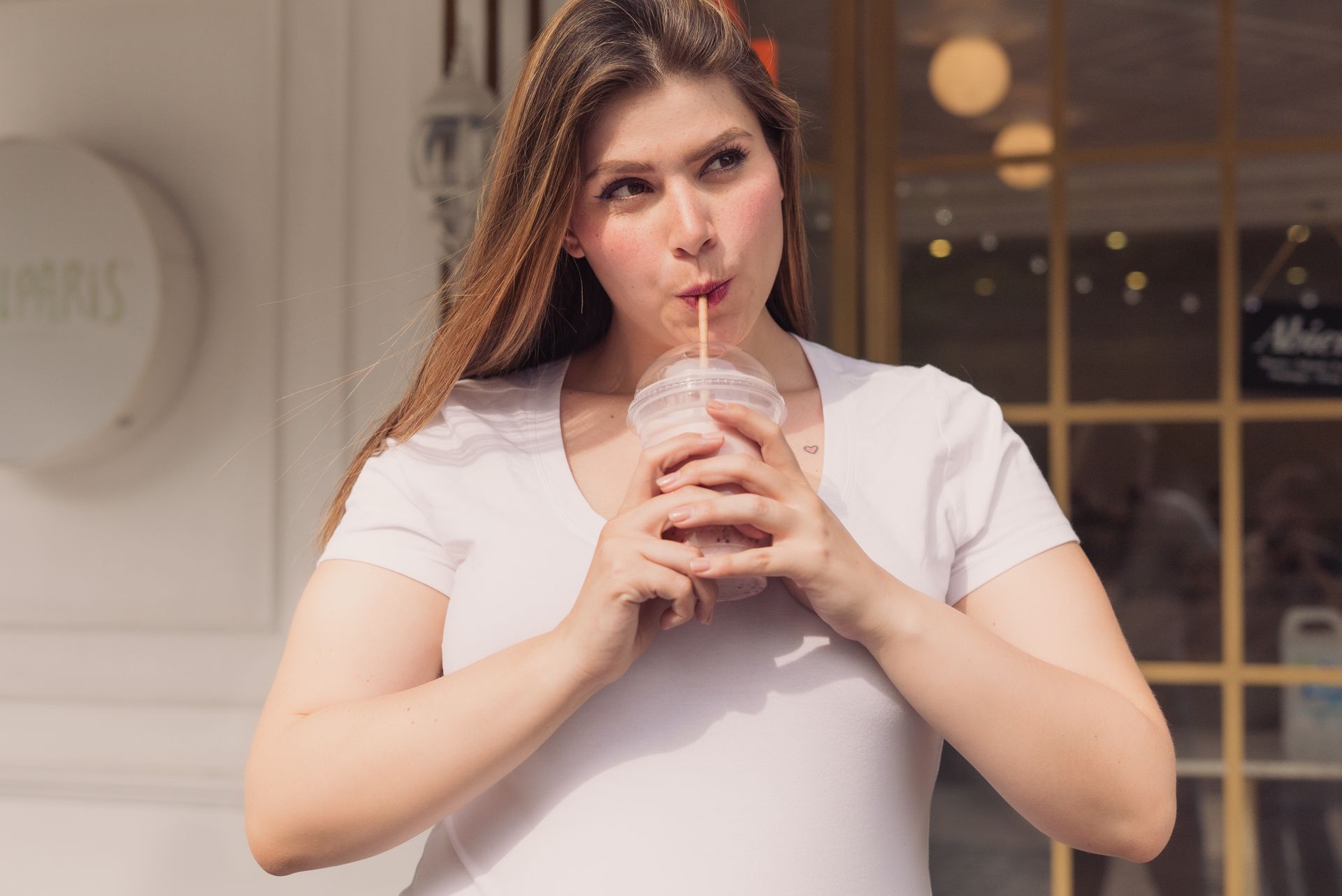 A joyful young woman sipping a refreshing drink outdoors on a sunny day.