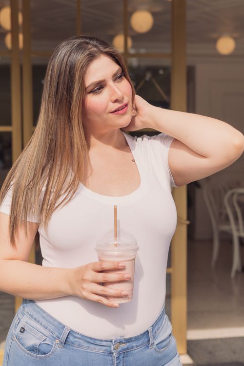 Free Plus size woman with long hair smiling, holding a drink and enjoying a sunny day outdoors. Stock Photo