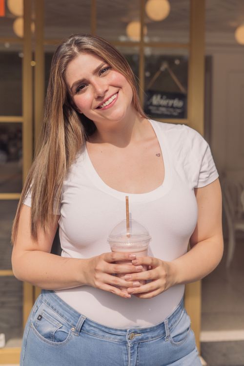 Free A cheerful woman holding a milkshake and smiling outdoors in an urban setting. Stock Photo