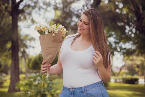 Free A cheerful woman holding a bouquet of flowers enjoys a sunny day in the park. Stock Photo