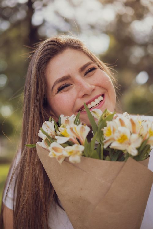 Free A joyful woman holding a bouquet of white and yellow flowers outdoors, exuding happiness. Stock Photo