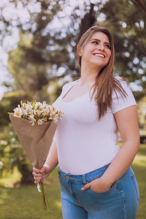 Free Happy woman with a flower bouquet smiling outdoors in a sunny park. Stock Photo