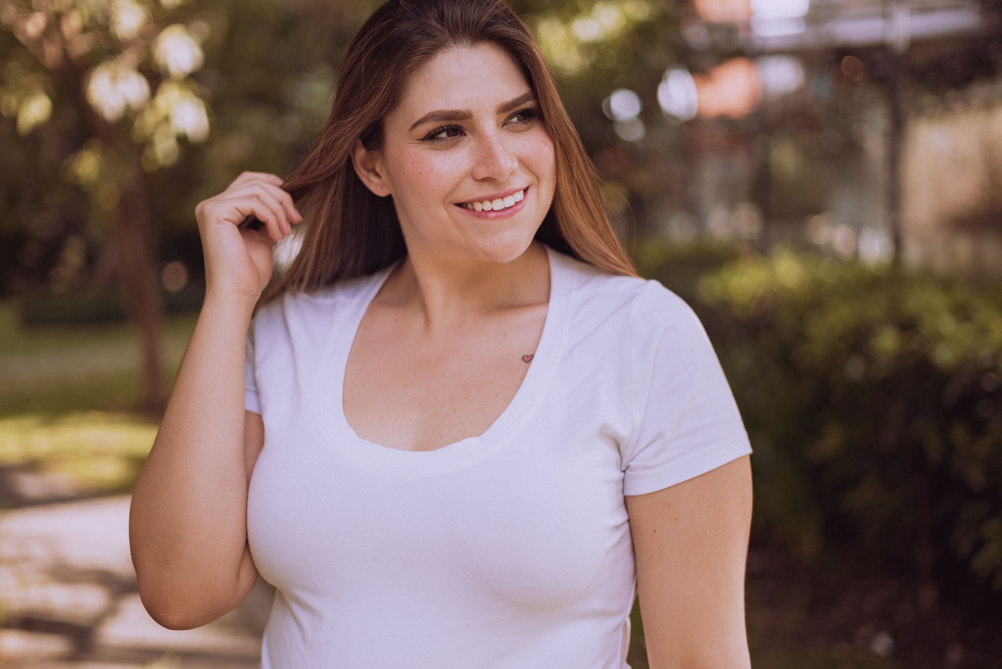A woman smiles while posing in a white shirt outdoors during the day.