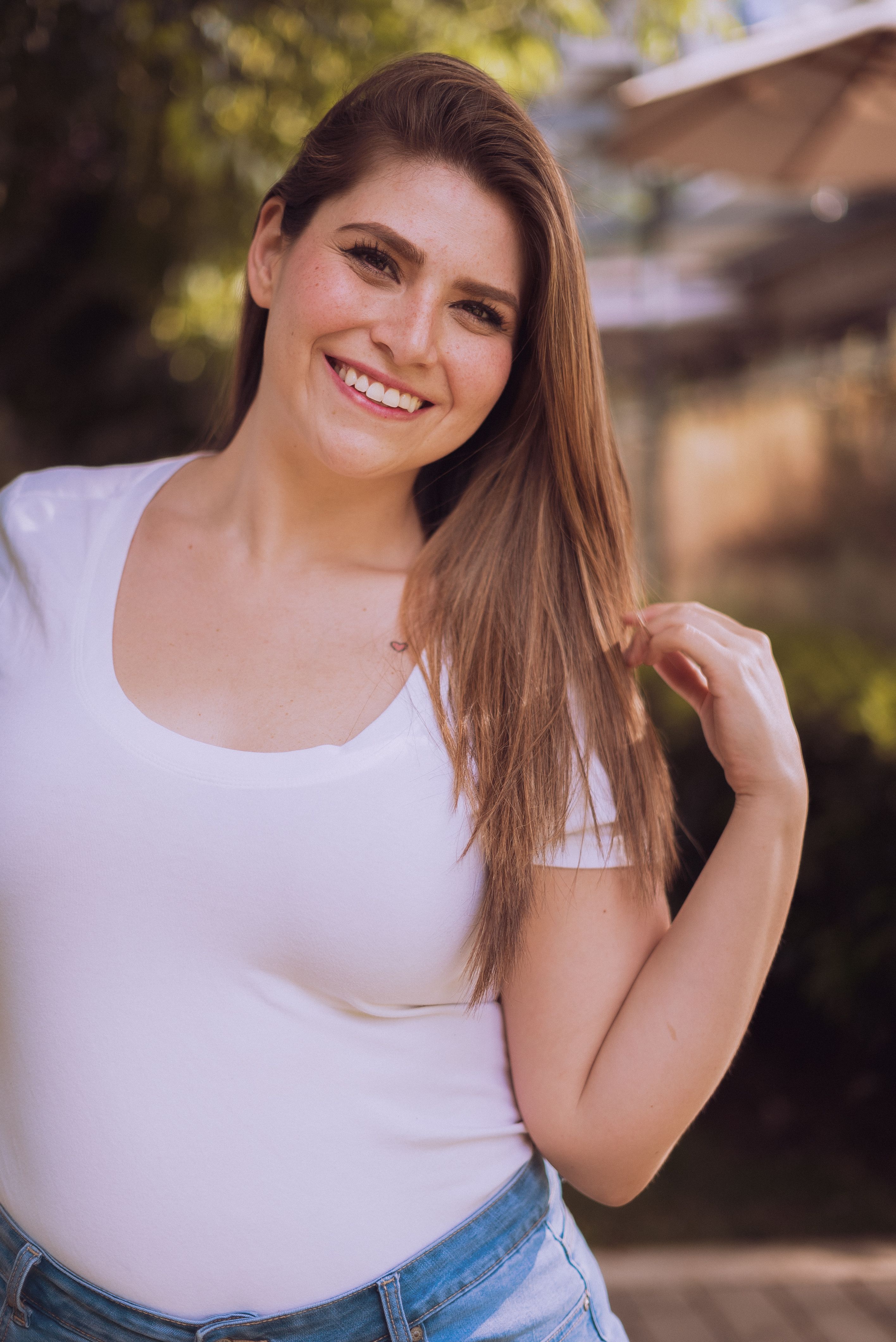 Confident woman in white shirt, smiling outdoors in sunny setting.