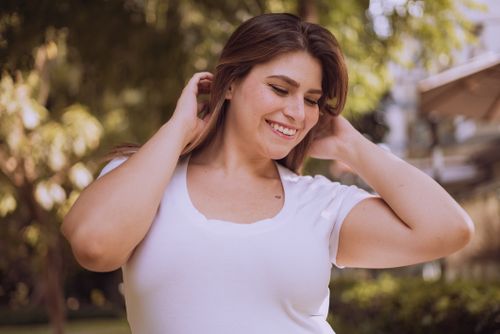 Free A cheerful plus-size woman in a white top, smiling outdoors with a natural background. Stock Photo