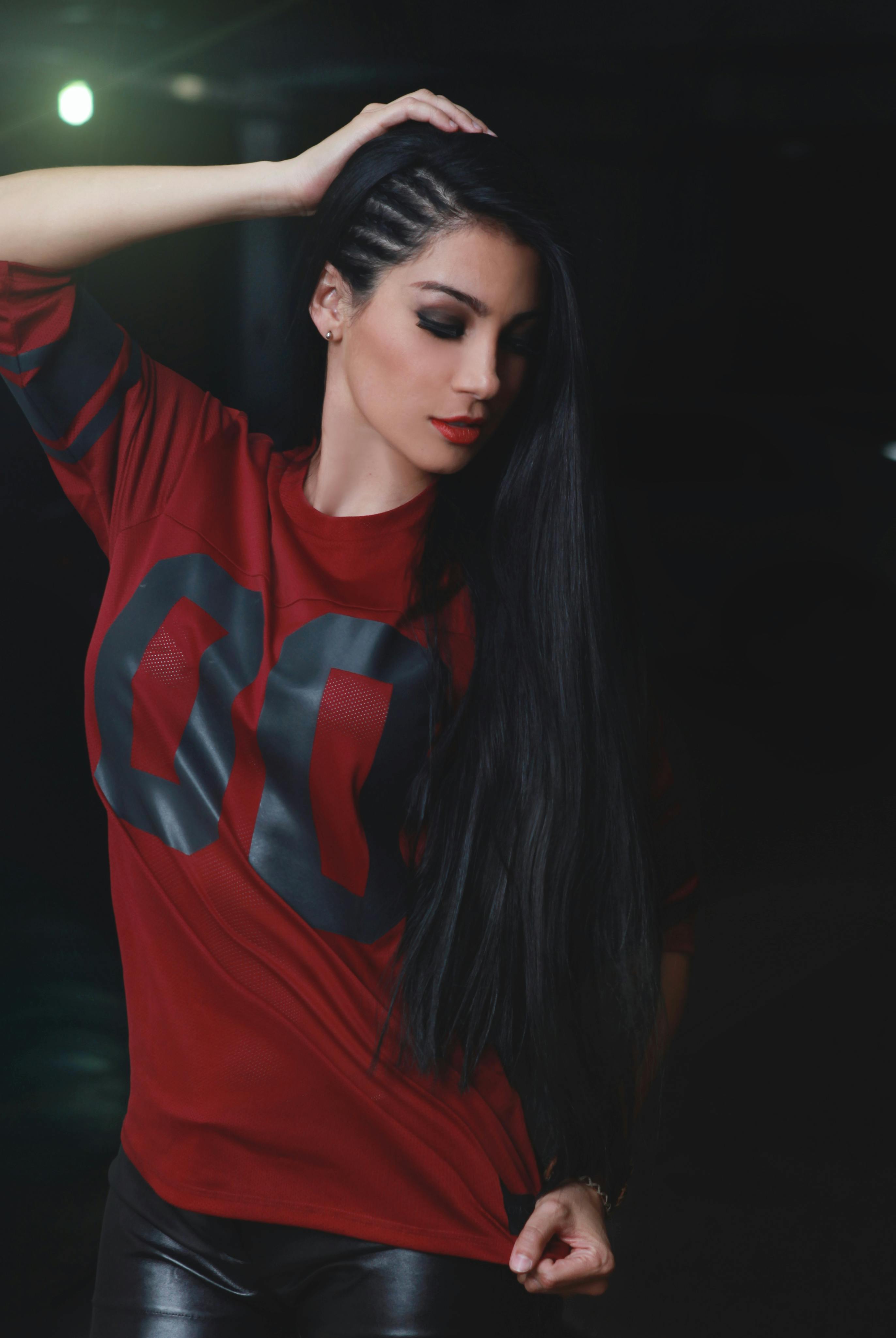 Free Elegant woman with long black hair posing in a red shirt against a dark background. Stock Photo