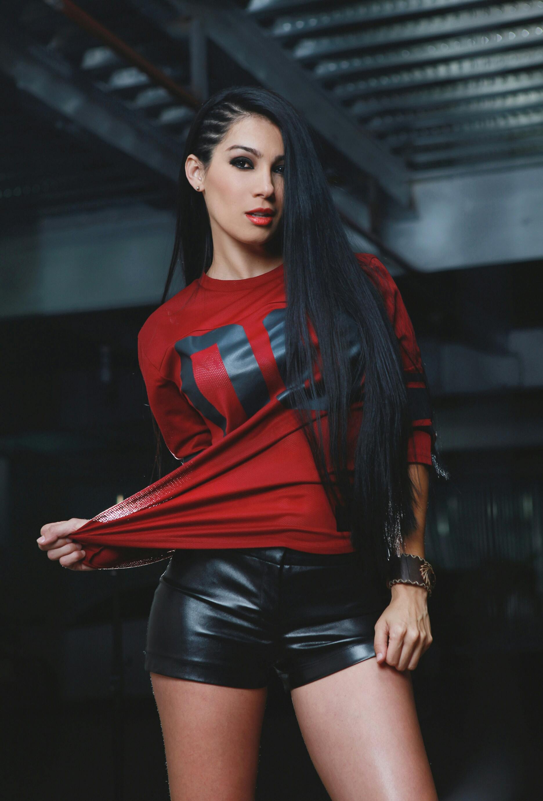 Confident woman posing in a modern setting with a red top and leather shorts, showcasing fashion and style.