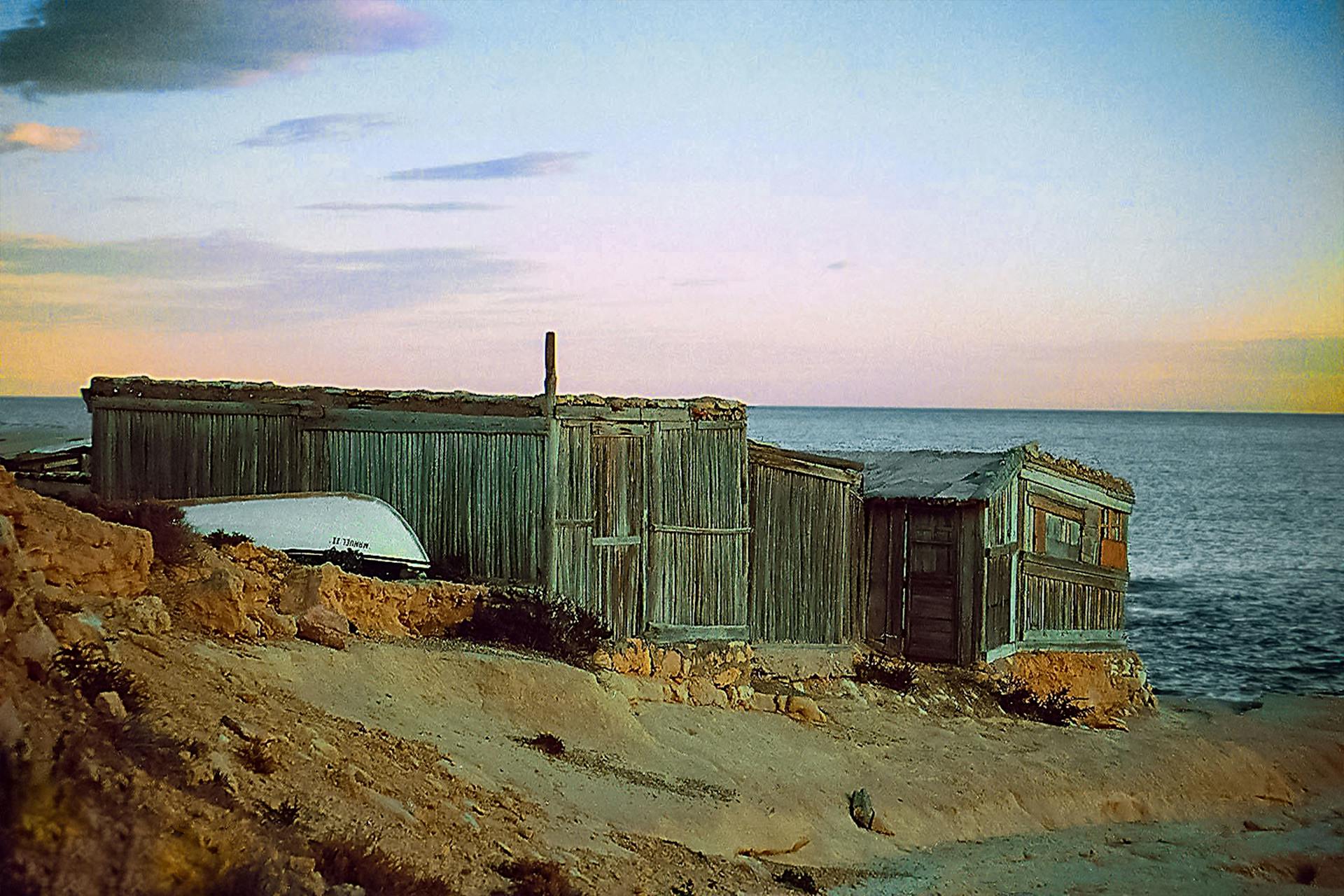 Rustic wooden shed on the Spanish coastline at sunset, capturing a serene seaside view.