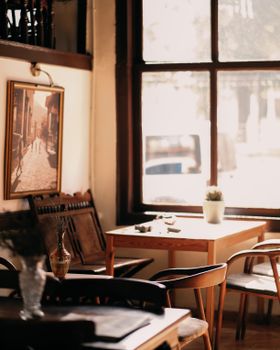 Sunlit cozy restaurant interior featuring wooden furniture and large window view.