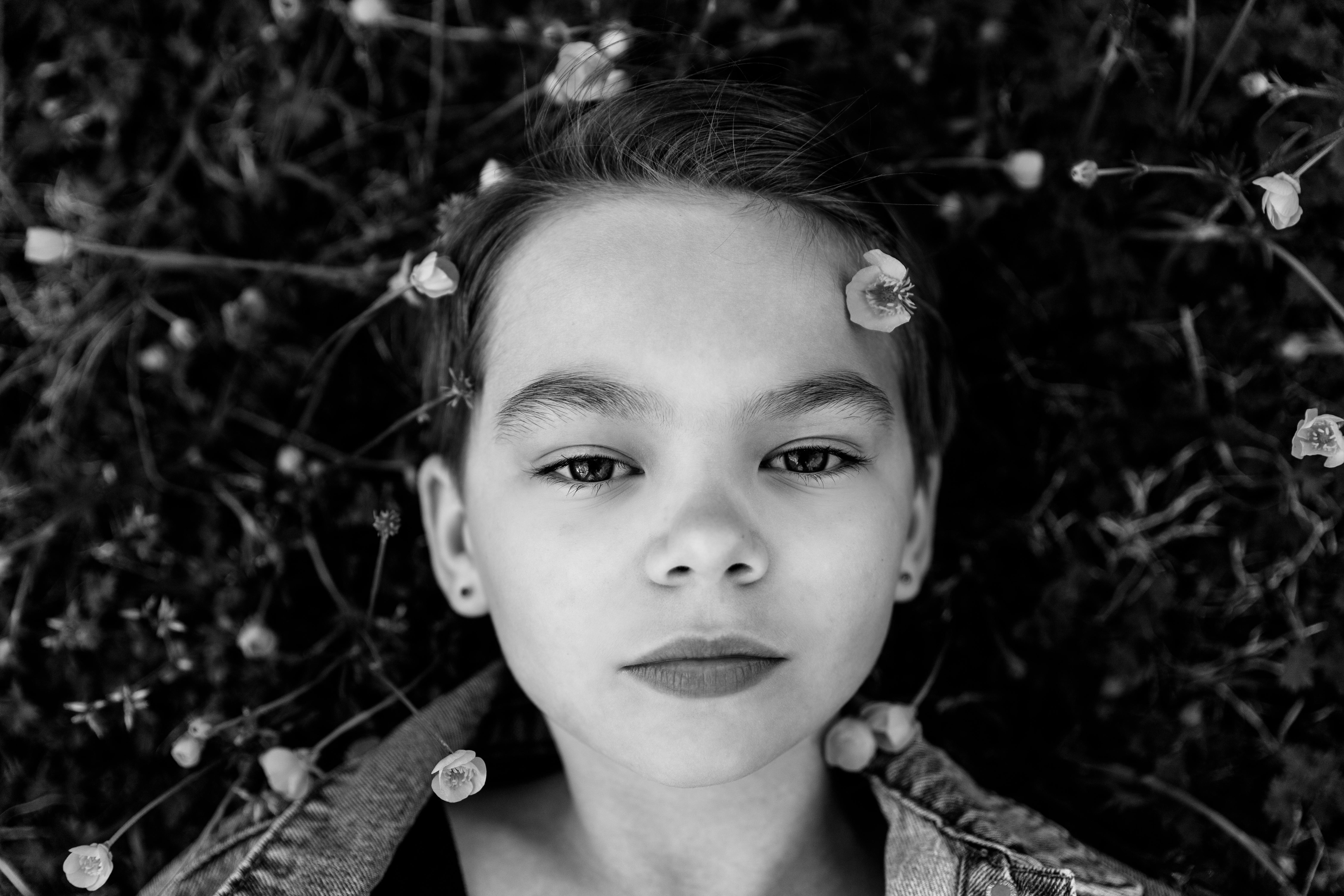 Grayscale portrait of a child lying down with flowers, conveying innocence.