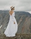 Back view of tender female in bridal dress and hat admiring majestic mountain with snow on wedding day