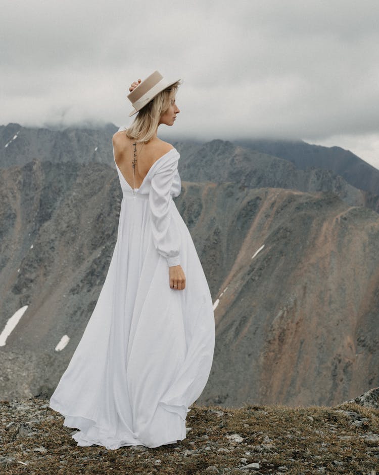 Elegant Bride In White Dress Contemplating Mount Under Cloudy Sky