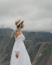 Elegant bride in hat admiring mounts on foggy day