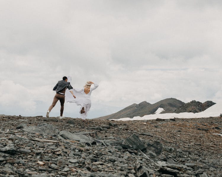 Faceless Newlywed Couple Running On Mount Under Cloudy Sky