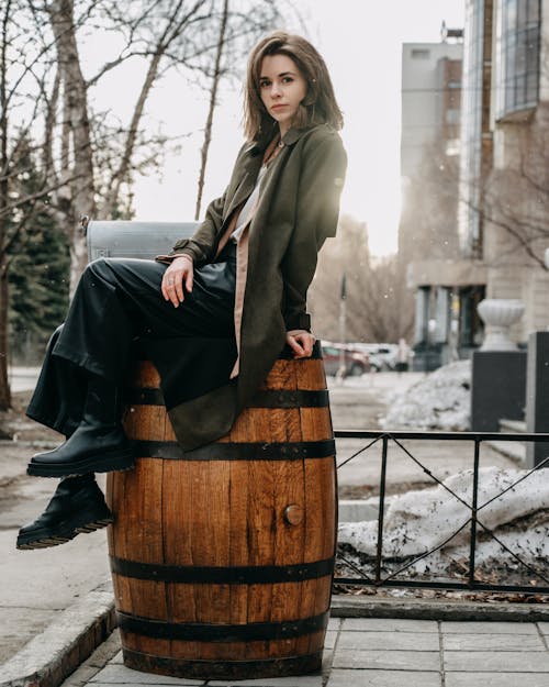 Stylish female sitting on decorative barrel on street in daytime